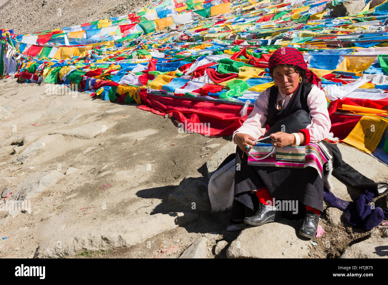 Tibetan nomad woman pilgrim sitting on rock, holding prayer beads in hand at Dolma La top en route Mt. Kailash Kora Stock Photo