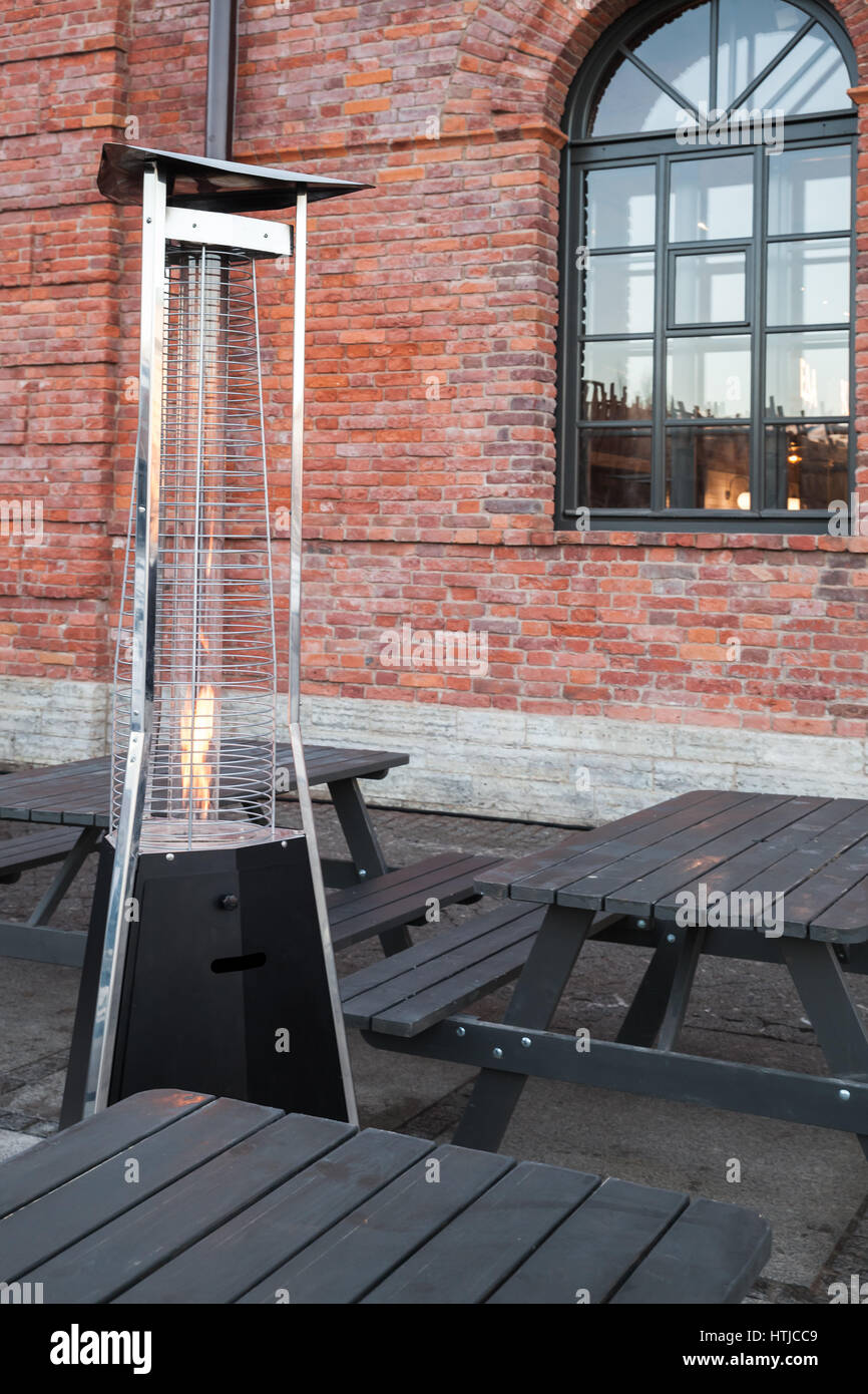 Outdoor gas heater stands near wooden tables on restaurant terrace Stock Photo