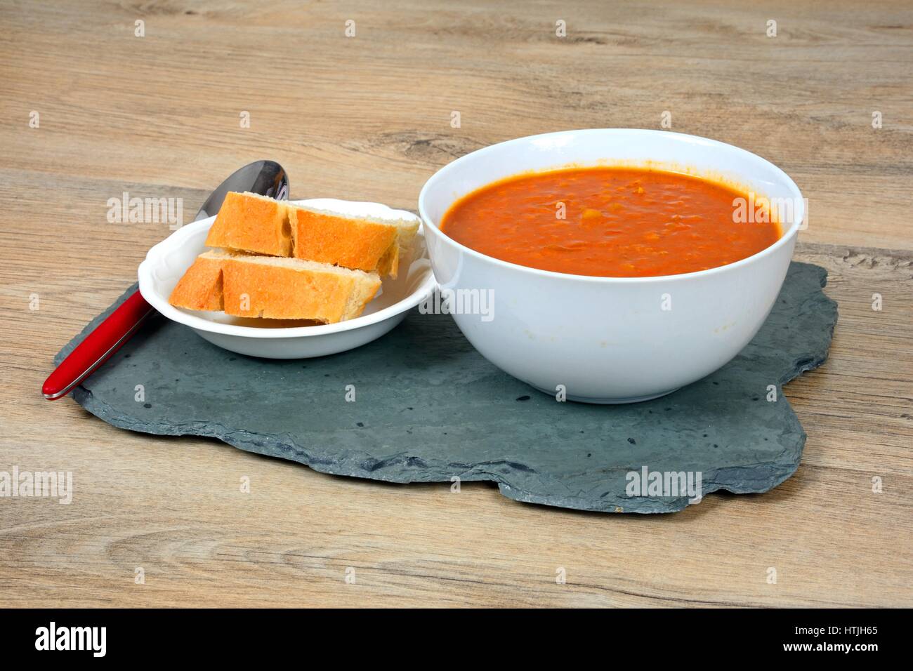 Spicy homemade vegetarian lentil, tomato vegetable soup with pieces of fresh bread, UK. Stock Photo