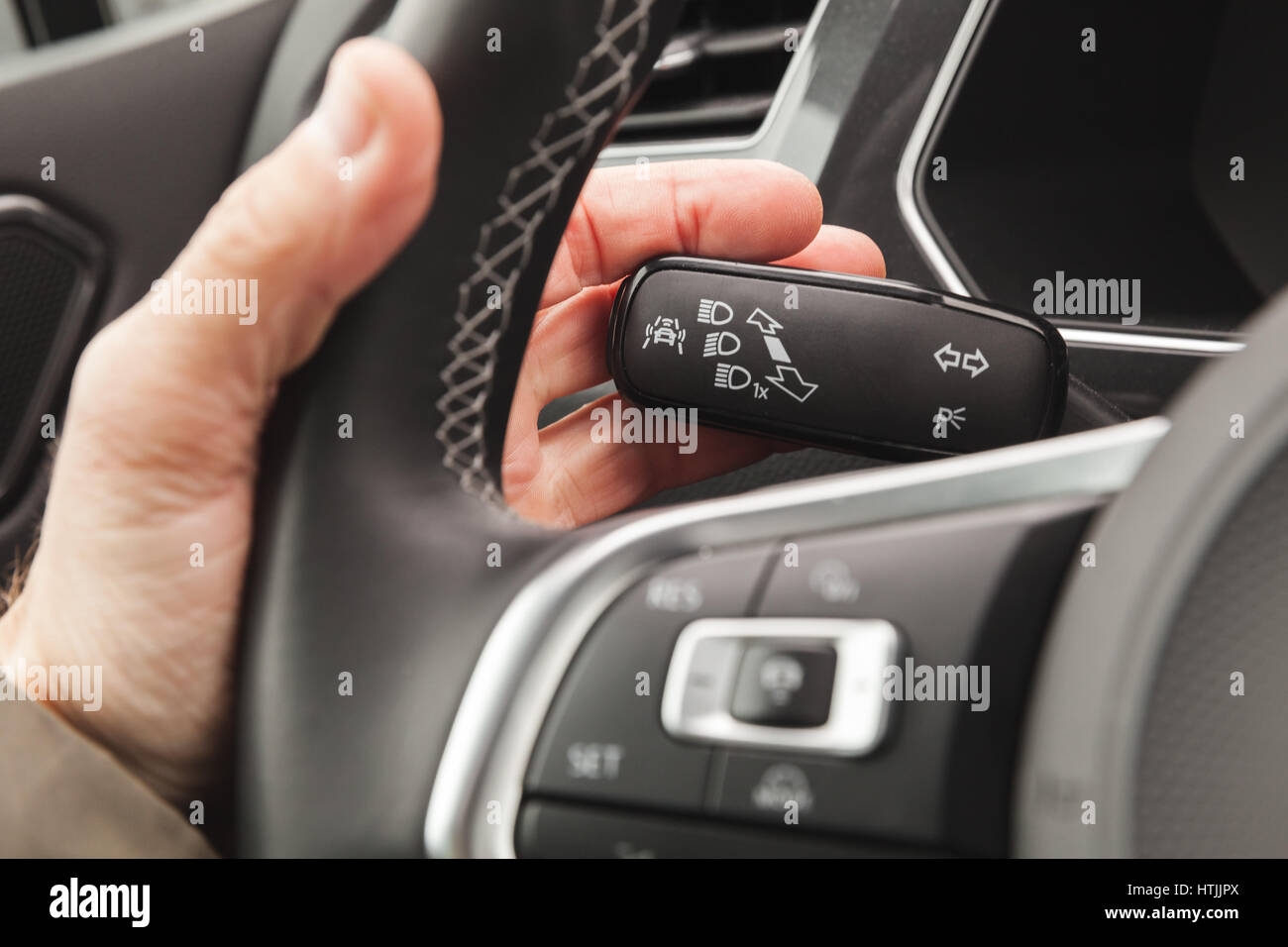 Driver hand pushing a headlights mode selector, modern crossover car interior details Stock Photo