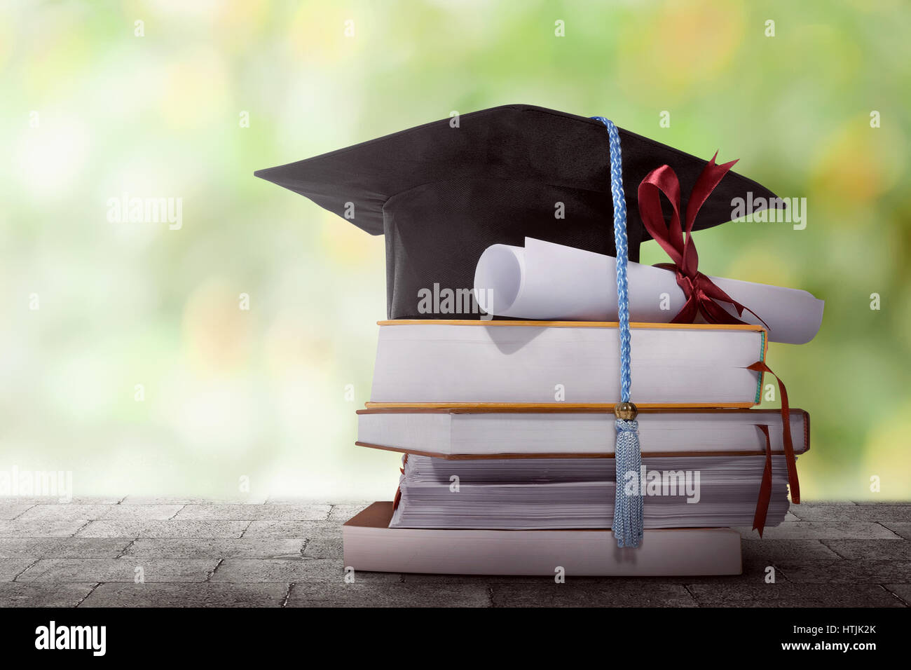 Graduation hat with degree paper on a stack of book against blurred background Stock Photo