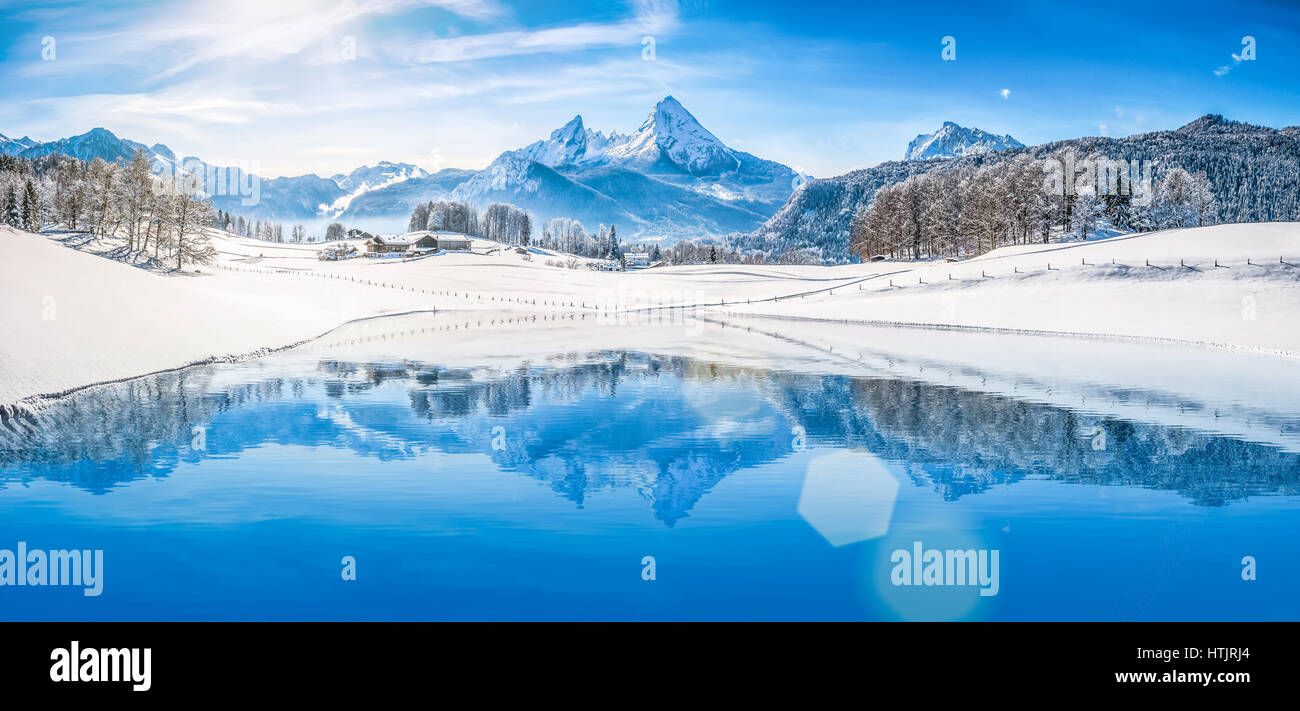 Panoramic view of beautiful white winter wonderland scenery in the Alps with snowy mountain summits reflecting in crystal clear mountain lake Stock Photo