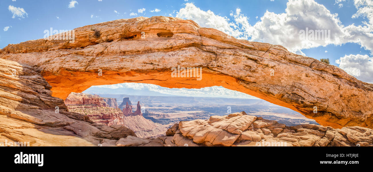 Panoramic view of famous Mesa Arch, iconic symbol of the American West, illuminated golden in beautiful morning light on a sunny day with blue sky and Stock Photo