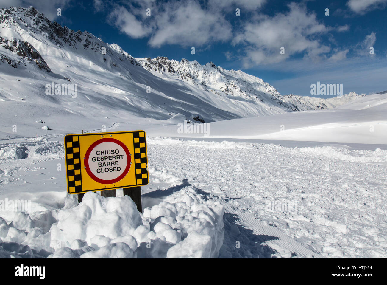 Sign saying ' Chiuso Gesperrt Barre Closed'. This relates to a closed mountain track due to heavy snow fall and avalanche risk in the Austrian Alps. Stock Photo