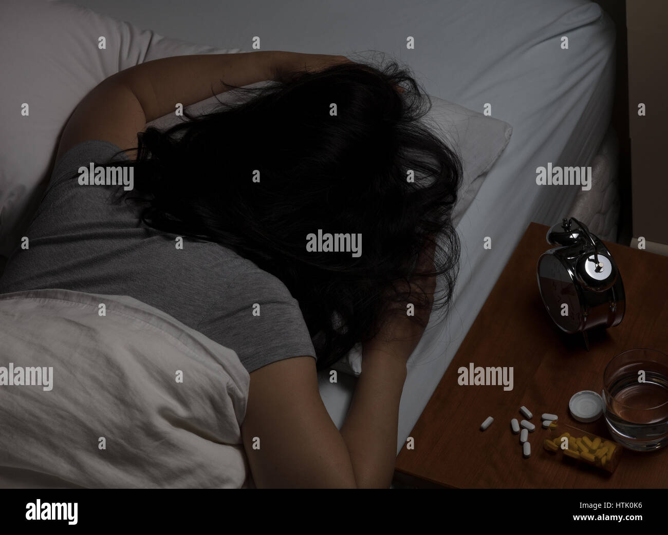 Woman lying face down in pillow with pills spilled on night stand. Depression and addiction concept. Stock Photo