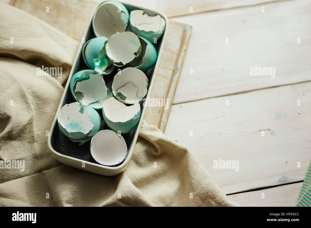 Plate full of blue tinted eggshells on white wooden table. Easter decoration. Stock Photo