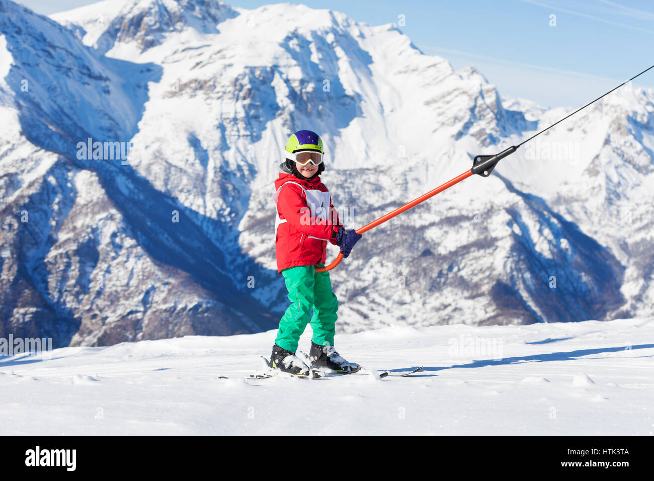 Smiling boy on a button ski lift going uphill in the mountains at sunny