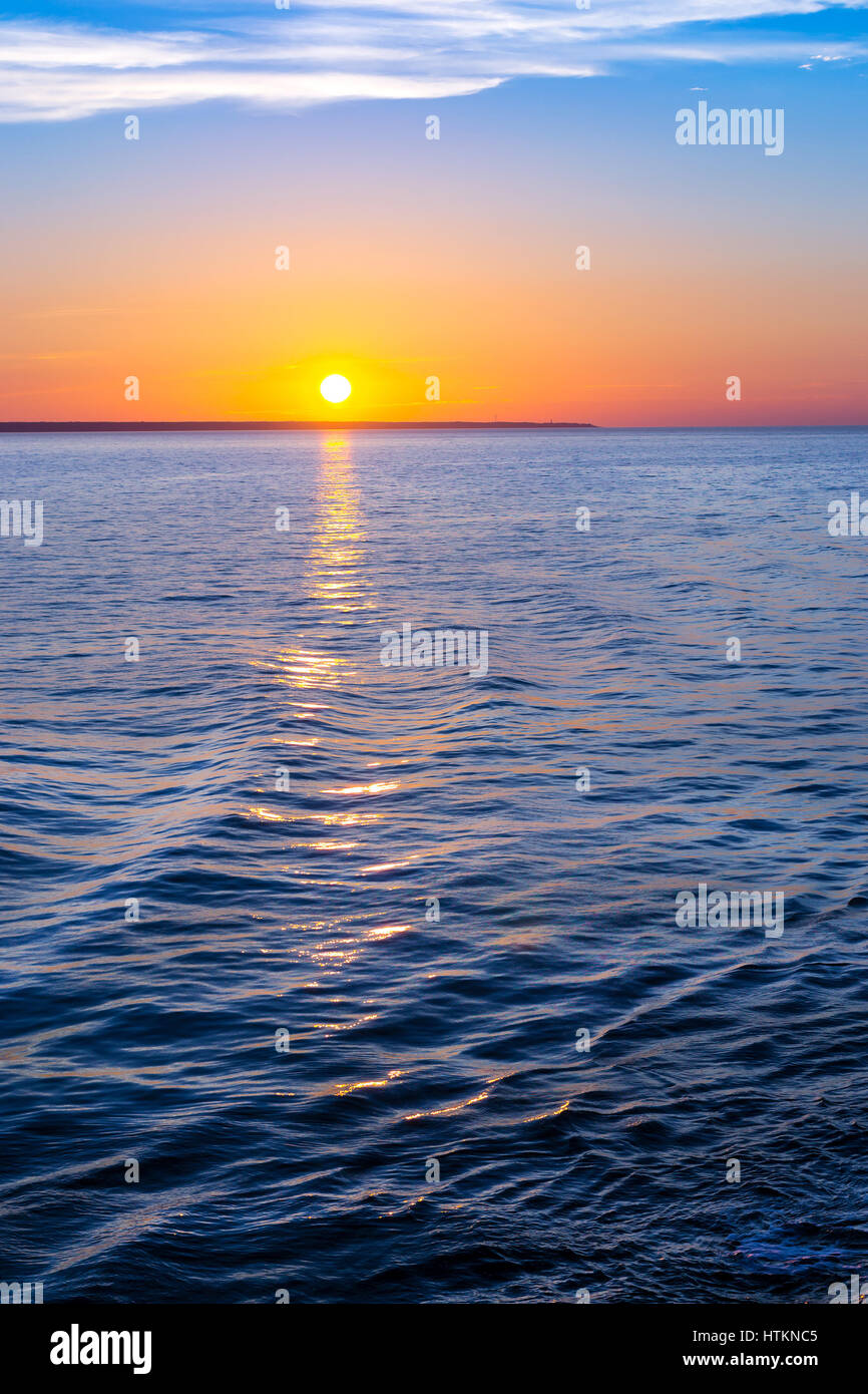 Sunset over sea horizon. Bright sun is reflected from water surface, evening sky with sparse Cirrus clouds. Sea Nordic walk on passenger ferry from He Stock Photo