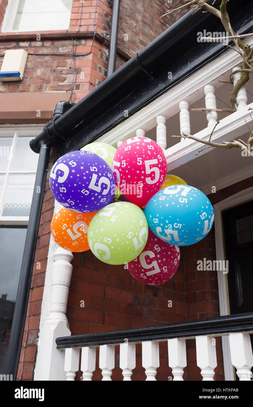 Bunch of multicoloured balloons for a five year old child's party hanging outside a house Stock Photo
