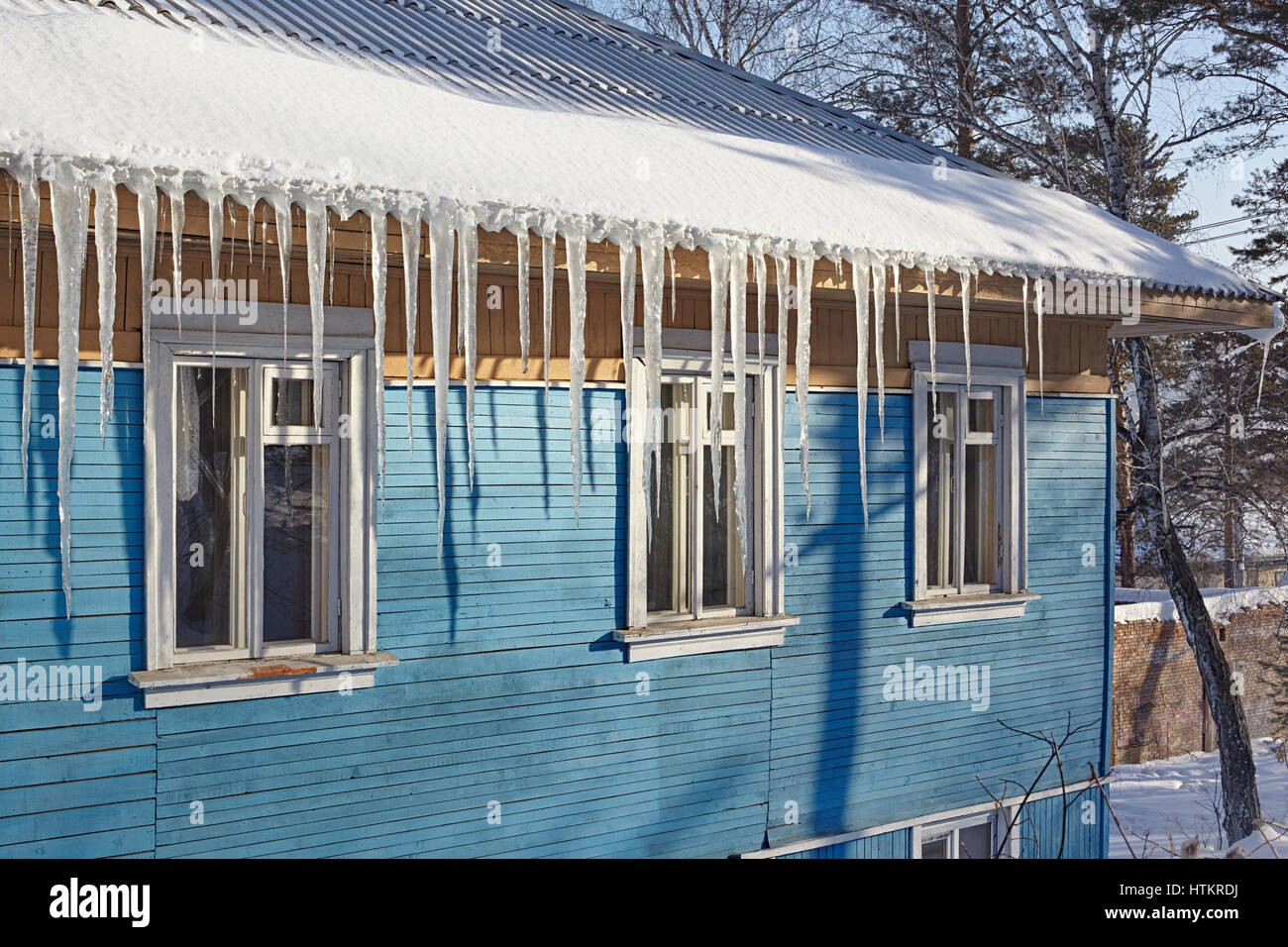 Dangerous icicles hanging from the roof of a wooden house Stock Photo