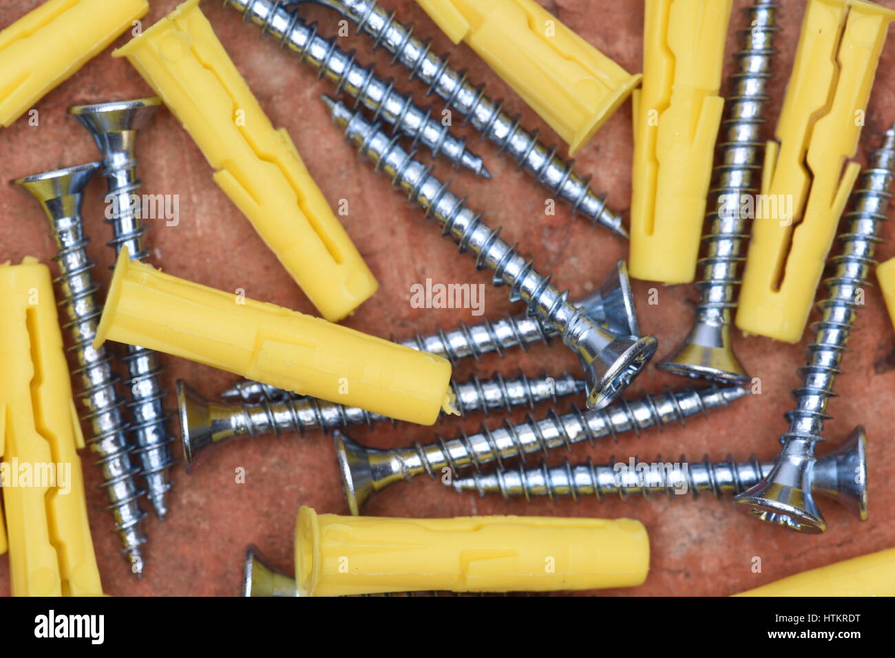 Plastic Dowels ans Screws on Red Brick Background Top View Stock Photo
