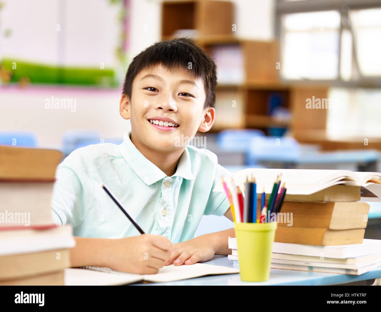 asian primary school student looking at camera smiling while studying in classroom. Stock Photo