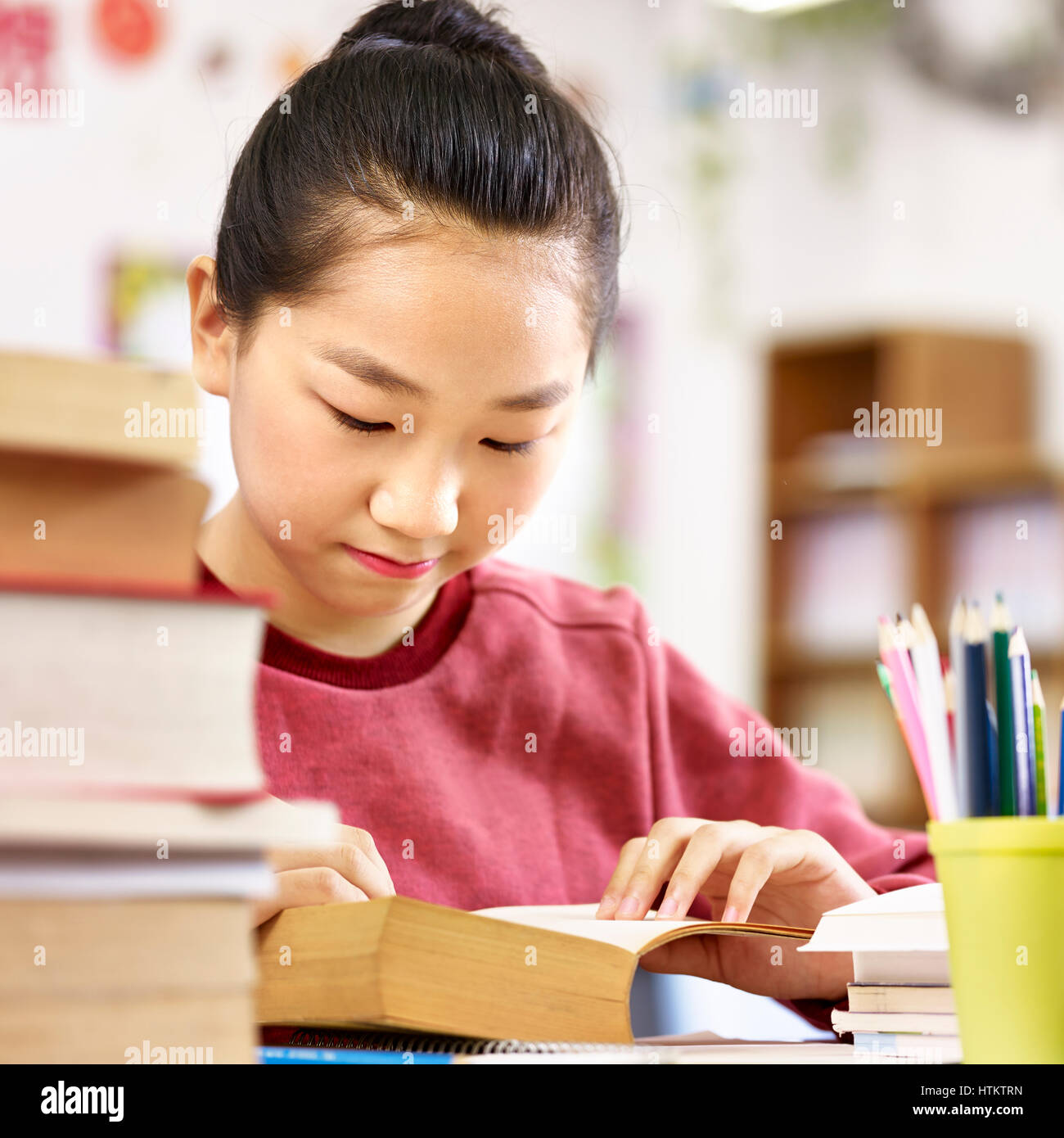 asian elementary schoolgirl reading a thick book in classroom. Stock Photo