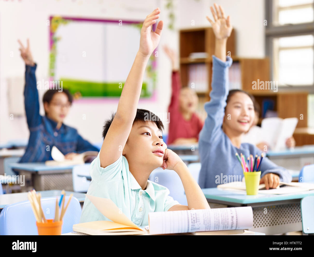 asian primary school pupils raising hands to answer questions in class. Stock Photo