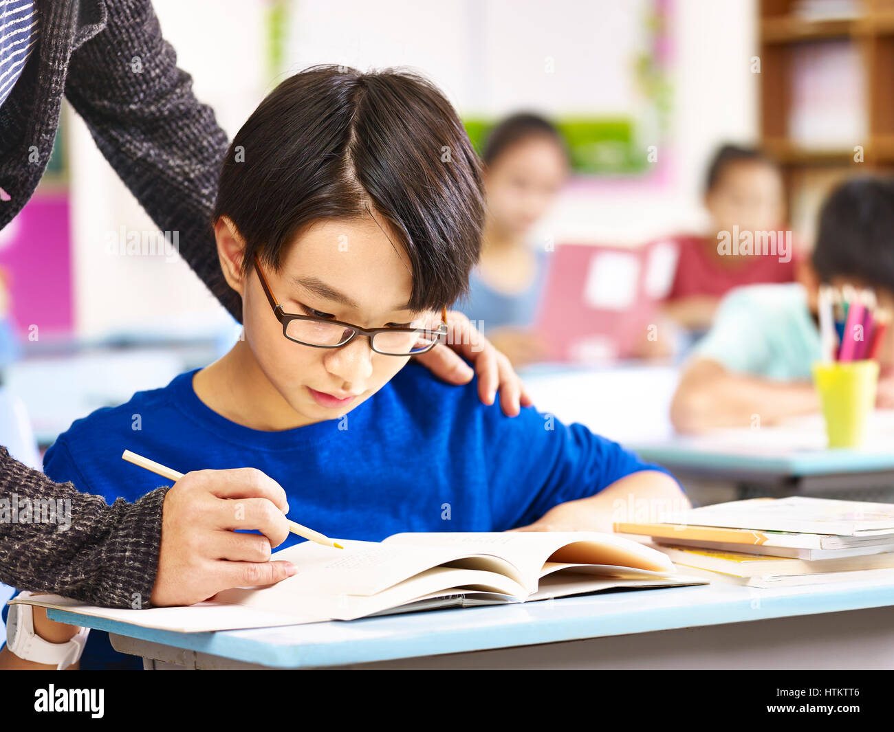 asian elementary school boy getting help from teacher in class. Stock Photo