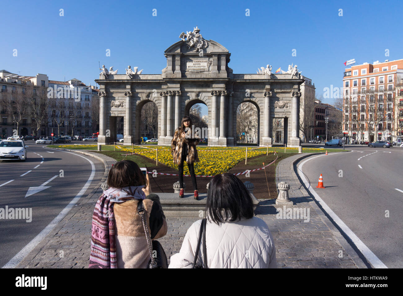 Tourist posing for a photograph in front of the Puerta de Alcalá, a triumphal arch in the Plaza de la Independencia, Madrid Stock Photo