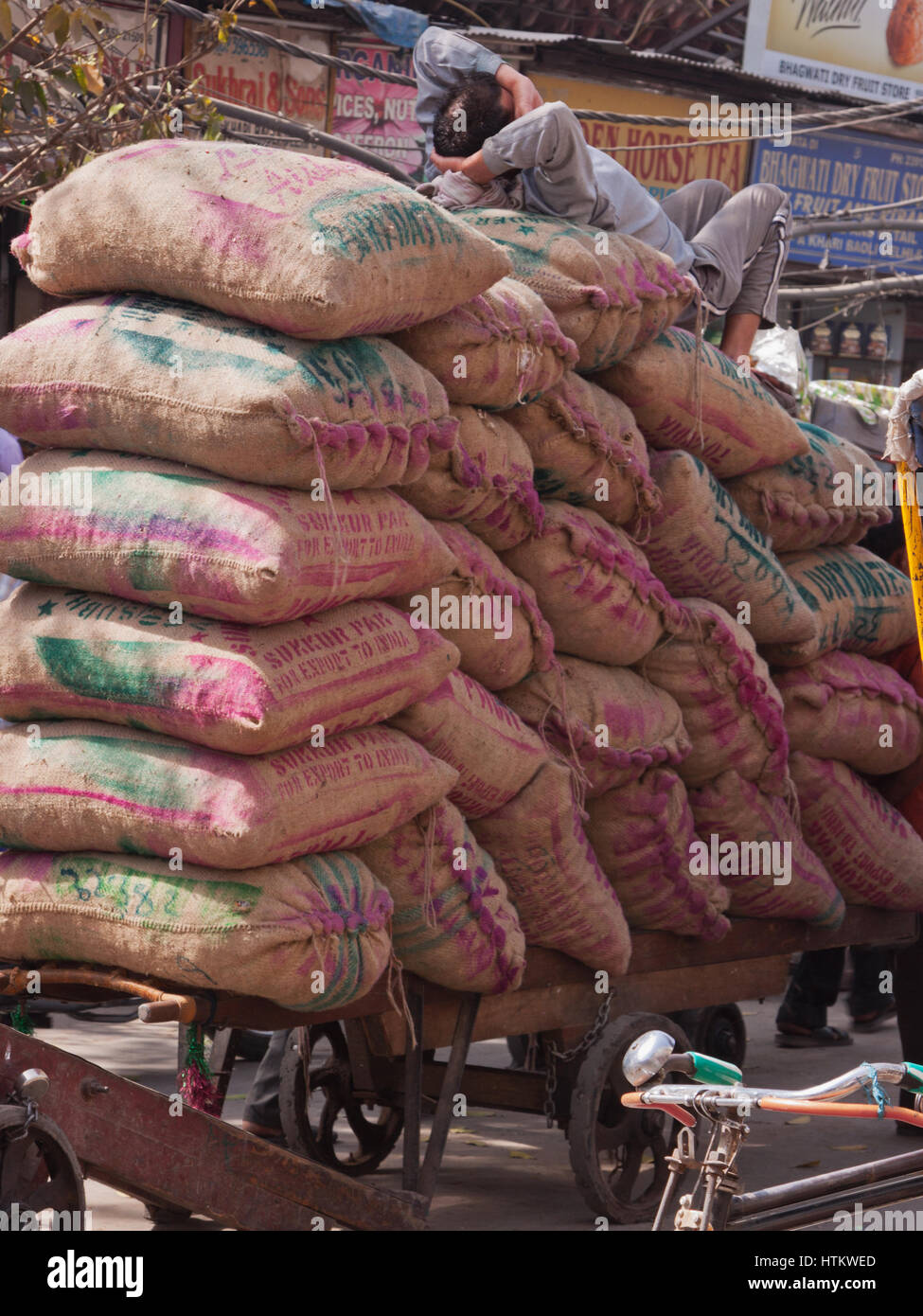 A worker resting on a cart full of grain sacks, taking an impromptu break from transporting goods in the heart of the old city of Delhi Stock Photo
