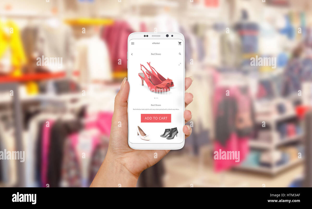 Online shopping with mobile phone. PHone in woman hand. Shop market online app on screen. Clothes and footwear shop in background. Stock Photo