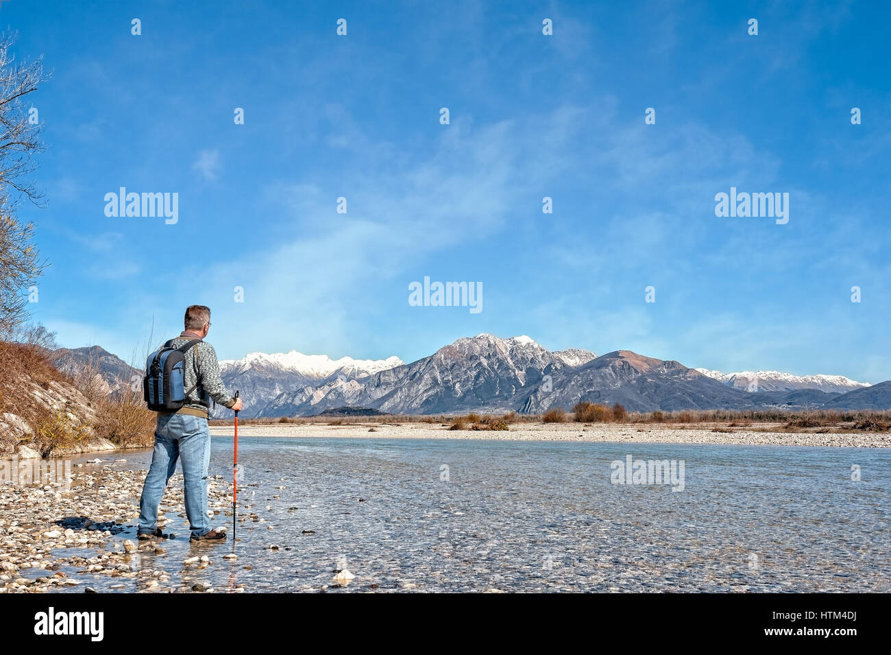 Mature hiker on the bank of a river. Trekking toward  mountain. Rambler about 60 years old. Active retirement. Copy space Stock Photo