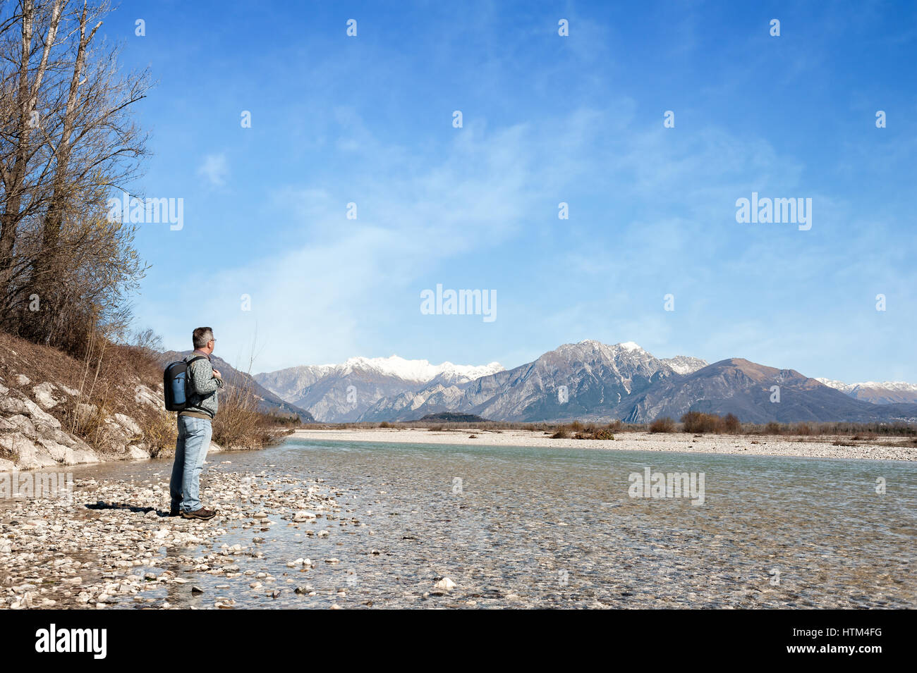 Mature hiker on the bank of a river. Trekking toward  mountain. Rambler about 60 years old. Active retirement. Copy space Stock Photo