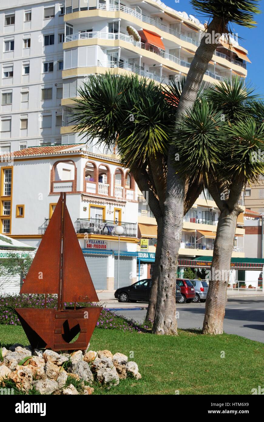 Metal boat sculpture on a traffic island with palm trees to the rear