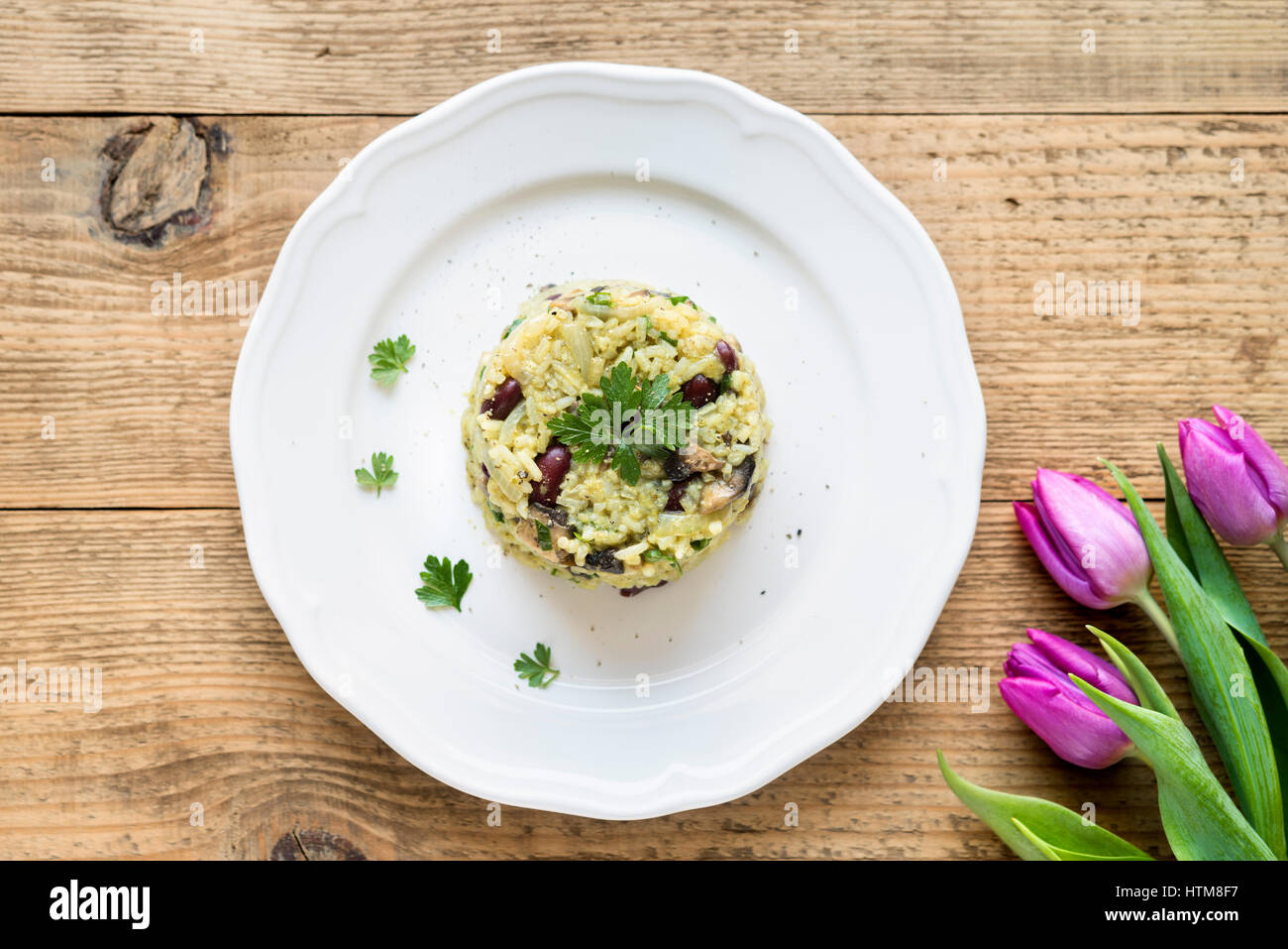 Top view of risotto (pilaf) with jasmine rice, red beans and vegetables on white plate on wooden rustic table Stock Photo