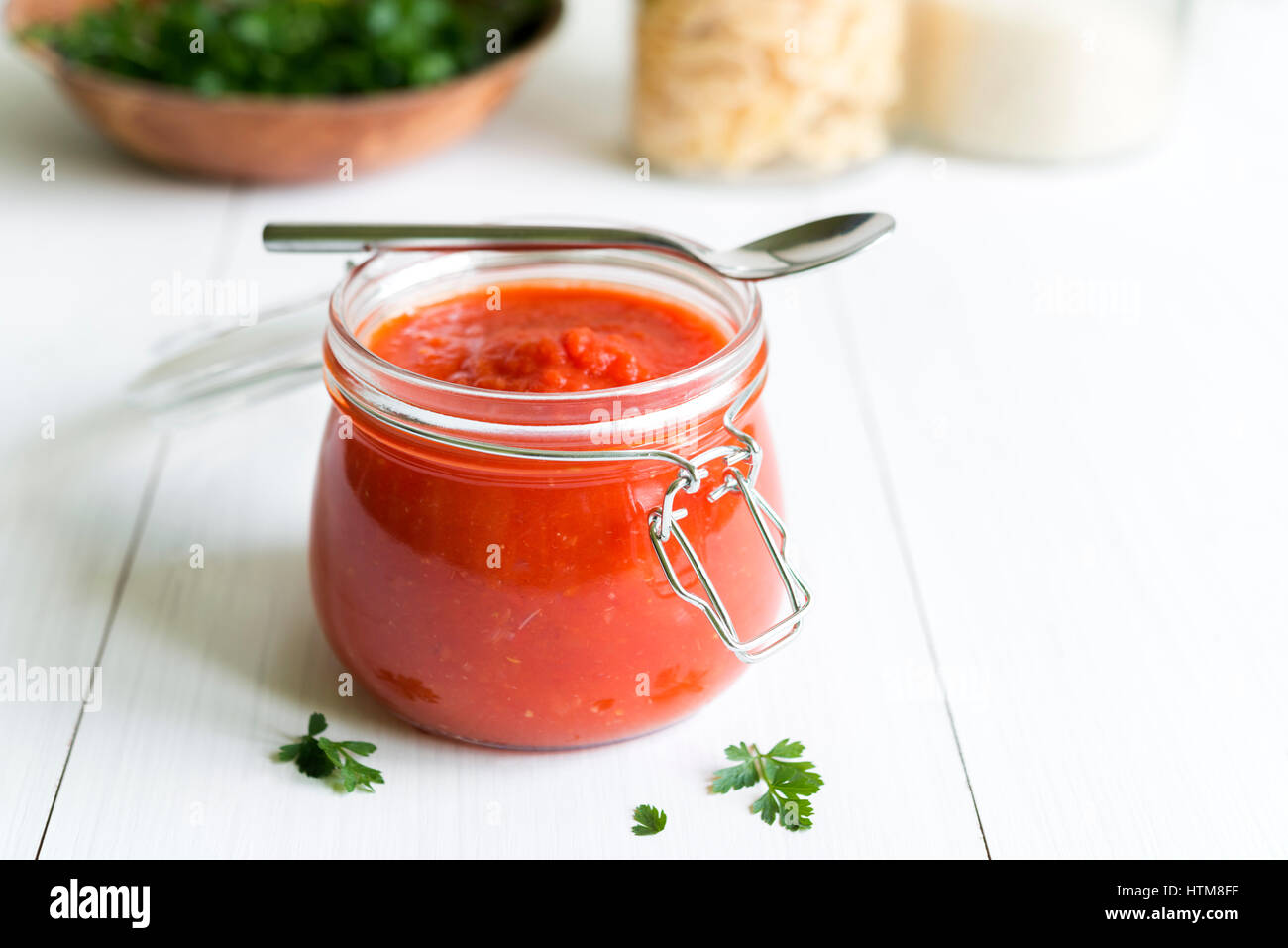 Jar of fresh homemade tomato sauce with parsley arranged on white wooden table. Stock Photo