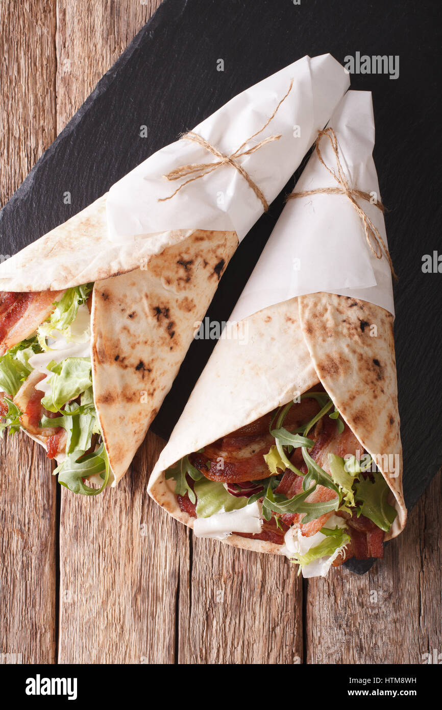 Fried bacon and salad wrapped in pita bread close-up on a table. Vertical view from above Stock Photo