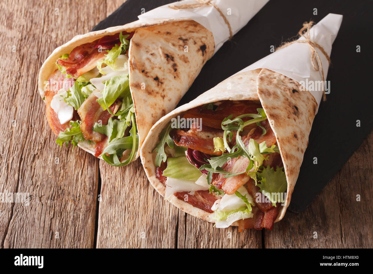 Fried bacon and salad wrapped in pita bread close-up on a table. horizontal Stock Photo