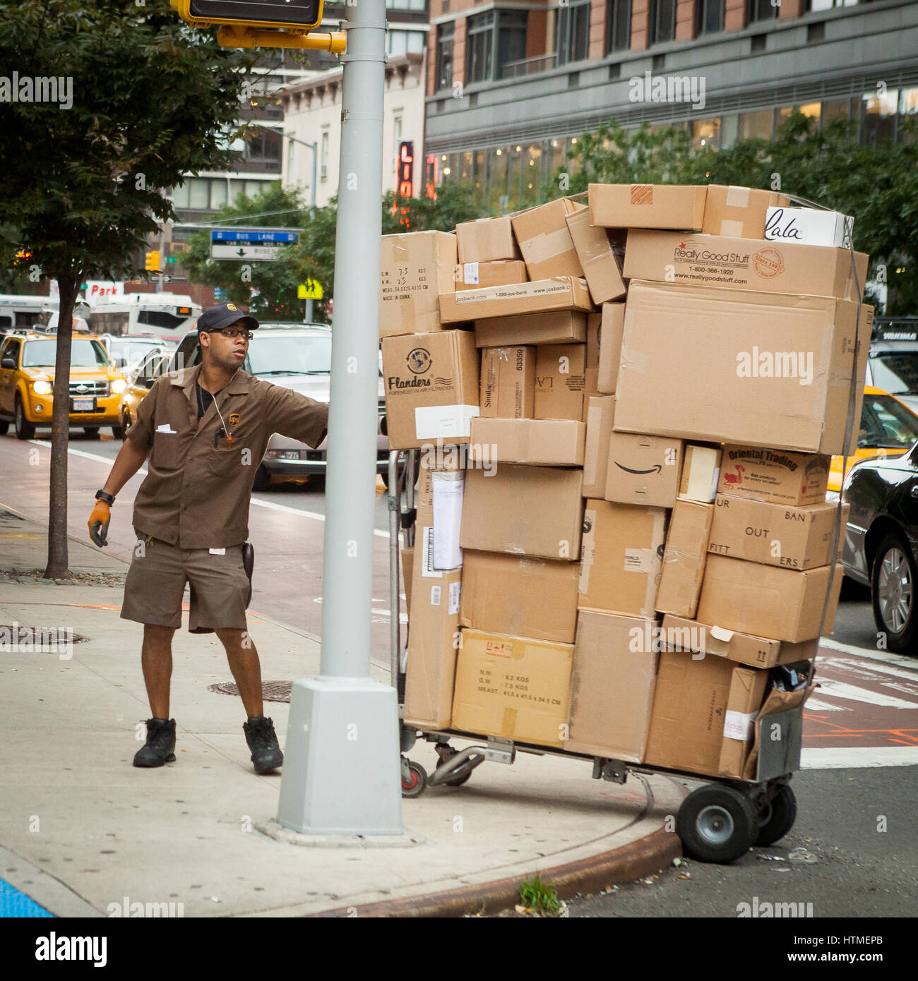 UPS (United Parcel Service) employee pulls a cart stacked high with packages over a curb during deliveries in New York City. Stock Photo