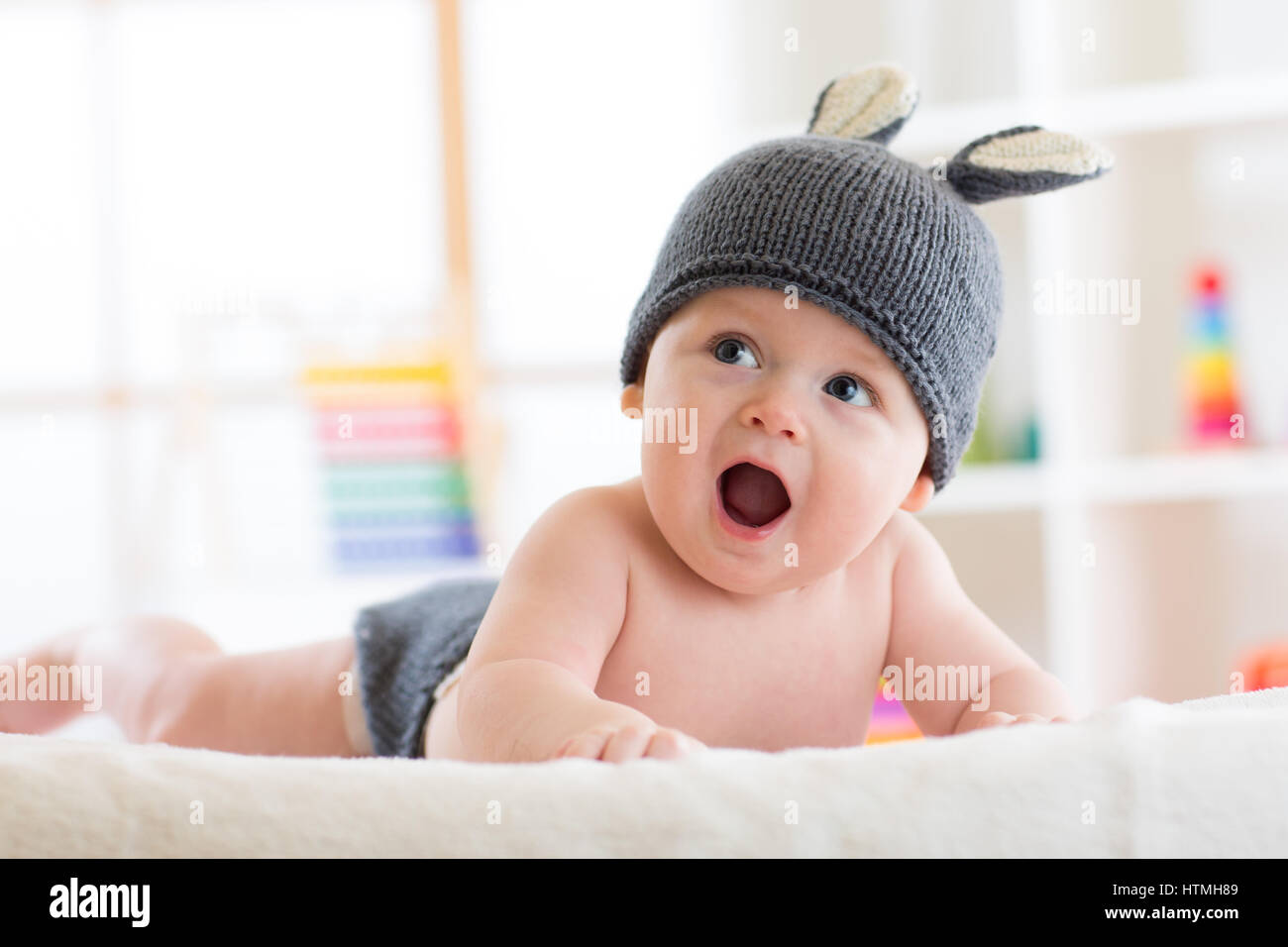 Smiling cute baby child in rabbit costume lying on bed in nursery Stock Photo