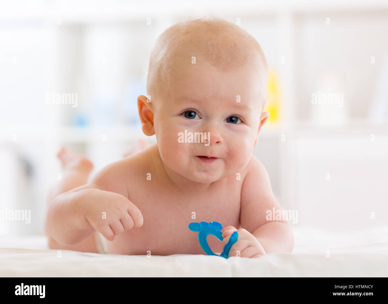 Portrait of adorable baby. Kid boy lying on his stomach and holding teether toy. Stock Photo