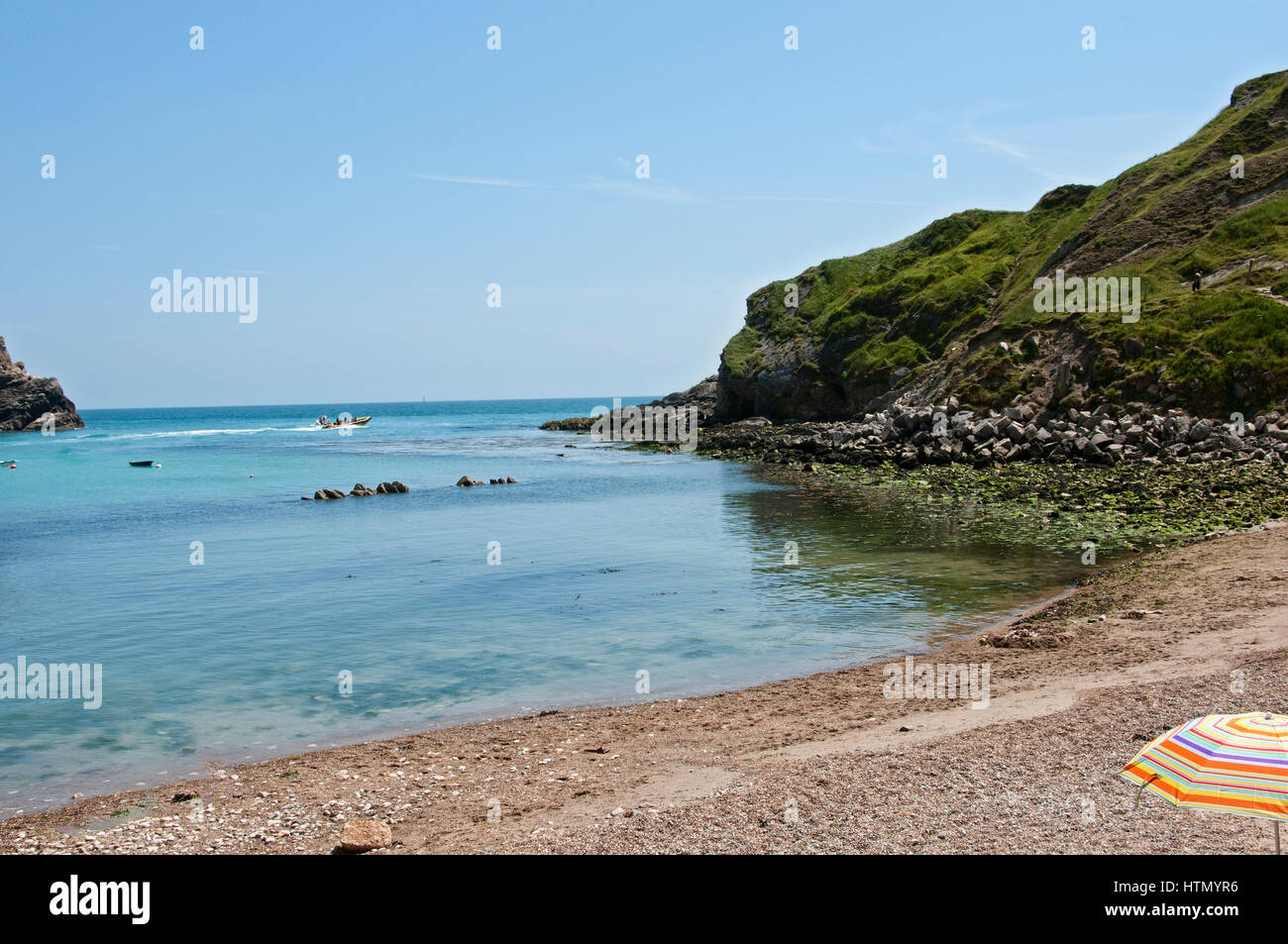 A single walker makes his way down a steeply dipping path towards the seashore as two boat trips sail out of Lulworth Cove between East and West Point Stock Photo