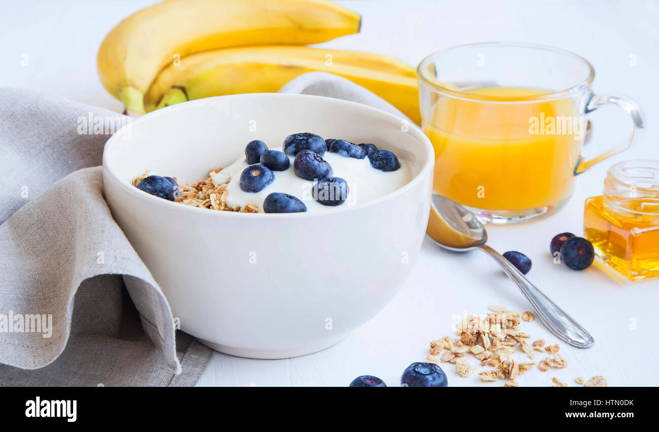 Granola with yogurt and blueberries, bananans and orange juice glass, healthy breakfast meal Stock Photo