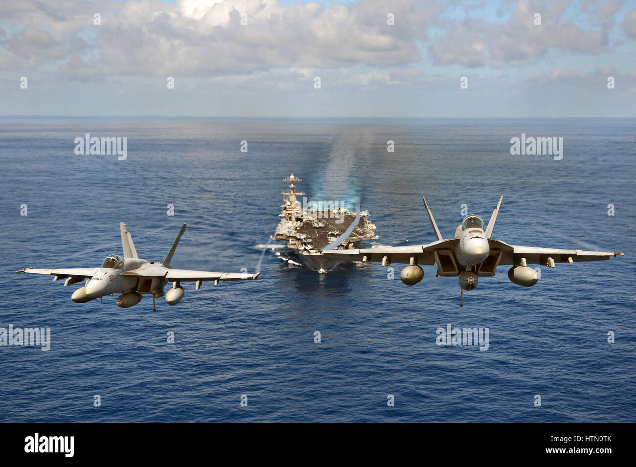 U.S. Navy F/A-18 Super Hornet fighter aircraft fly in formation in front of the USN Nimitz-class aircraft carrier USS John C. Stennis April 24, 2013 in the Pacific Ocean. Stock Photo