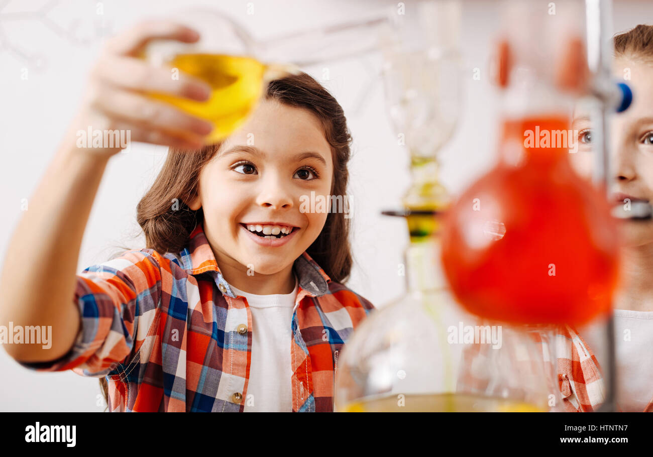 Exited about the experiment. Nice happy positive girl smiling and holding a flask while being excited about the chemical experiment Stock Photo