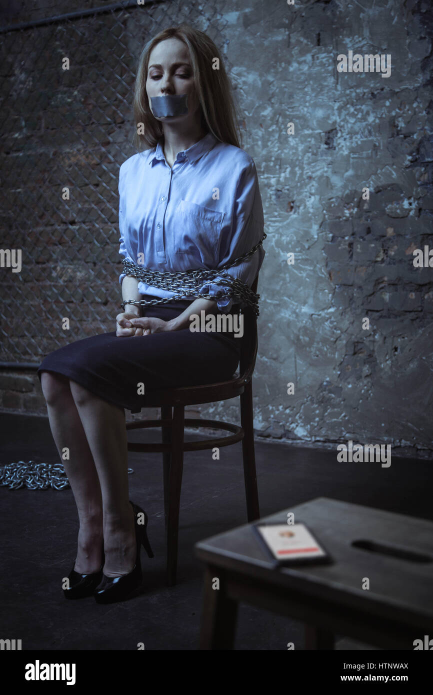 Police, maybe. Scared frozen captured woman trying looking at who calling her while being kidnapped and sitting tied up to a chair Stock Photo