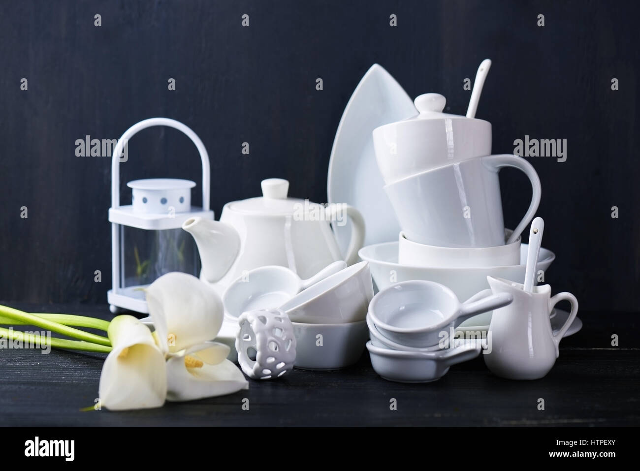 Set of new white dishes with teapot, tea cups, and plates on a black