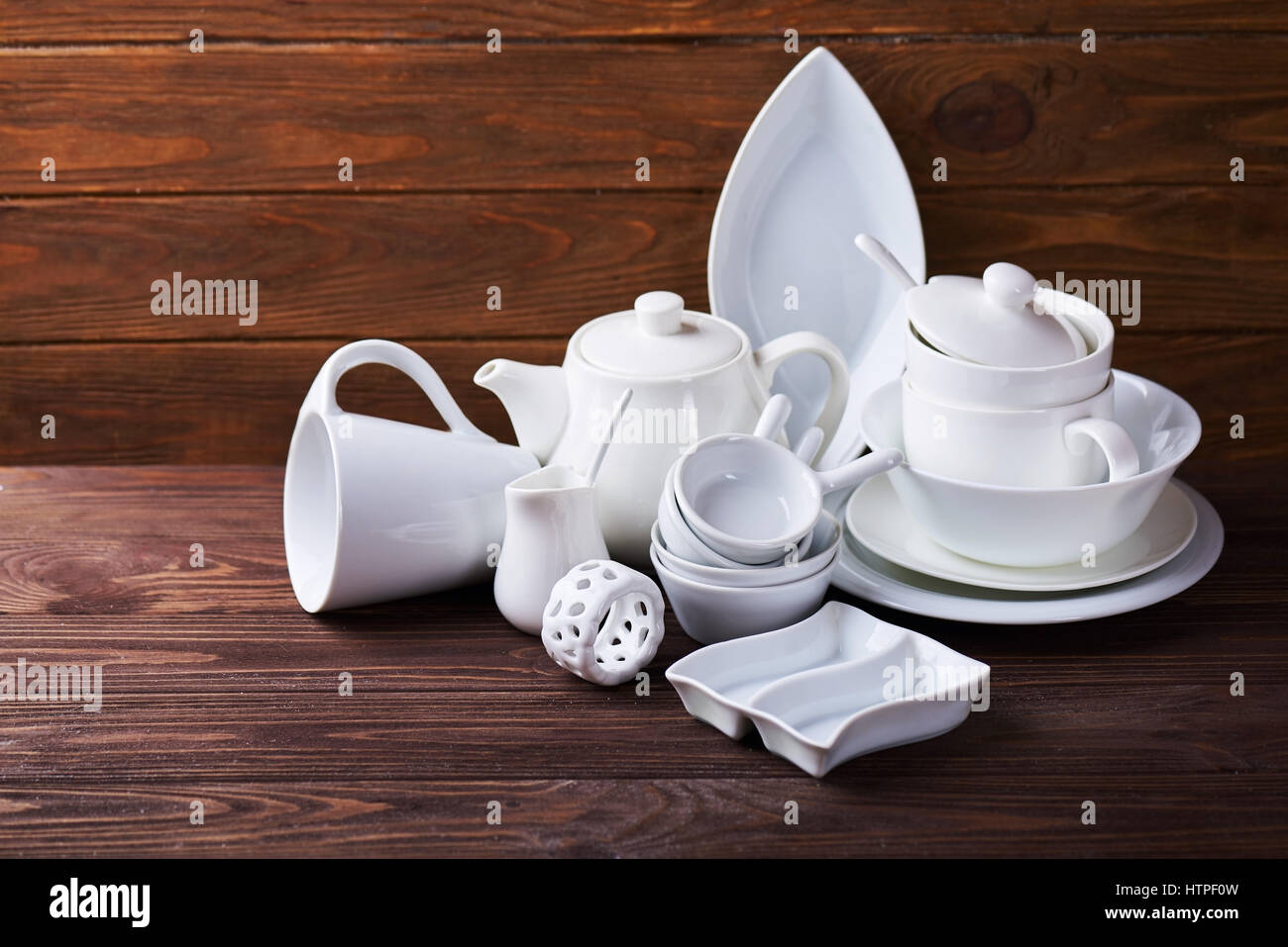 Set of new white dishes with teapot, tea cups, and plates on wooden