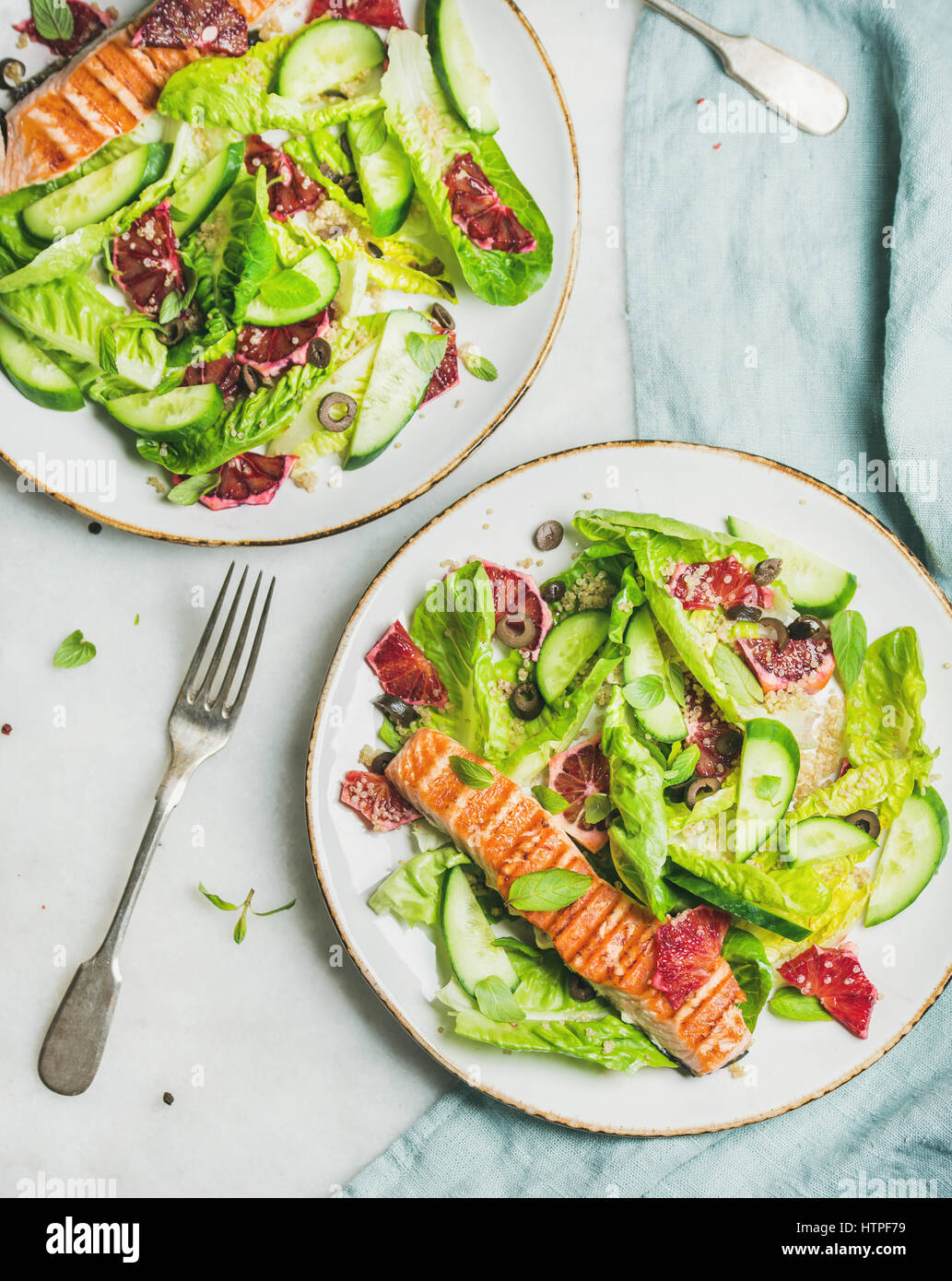 Healthy energy boosting spring salad with grilled salmon, blood orange, olives, cucumber and quinoa in white plates, top view, marble background. Clea Stock Photo