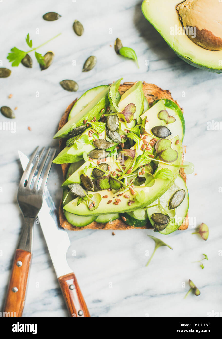 Healthy green veggie breakfast concept. Sandwich with avocado, cucumber, kale, kress sprouts, pumpkin seeds over marble background, top view. Vegan, w Stock Photo