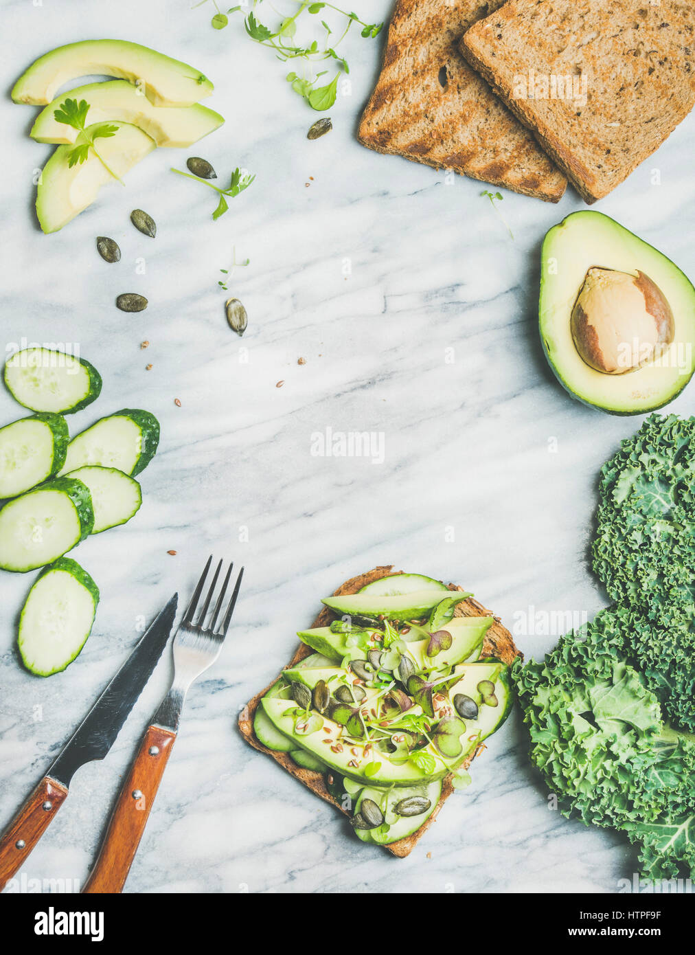 Healthy green veggie breakfast concept. Sandwich with avocado, cucumber, kale, kress sprouts and pumpkin seeds over marble background, top view, copy Stock Photo