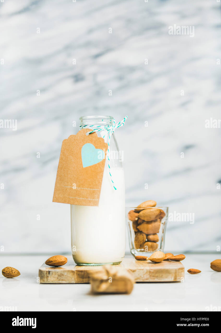 Fresh vegan dairy-free almond milk in glass bottle with craft paper label with copy space, grey marble background, selective focus. Vegan, vegetarian, Stock Photo