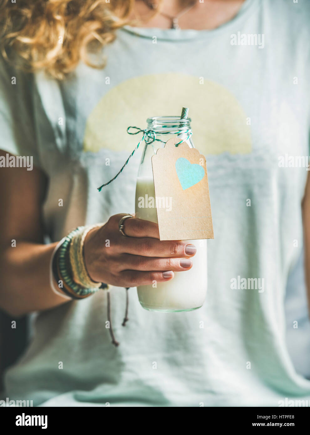 Young blond woman in grey light holding bottle of dairy-free almond milk in her hand. Clean eating, vegan, vegetarian, dieting, healthy food concept Stock Photo