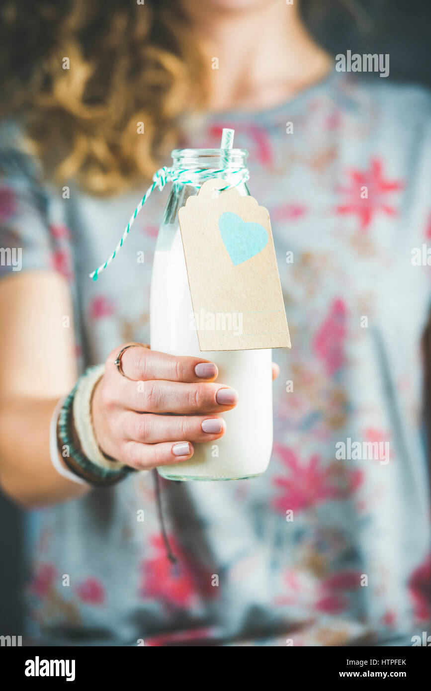 Young blond woman in grey t-shirt with floral pattern holding bottle of dairy-free almond milk in her hand. Clean eating, vegan, vegetarian, dieting, Stock Photo