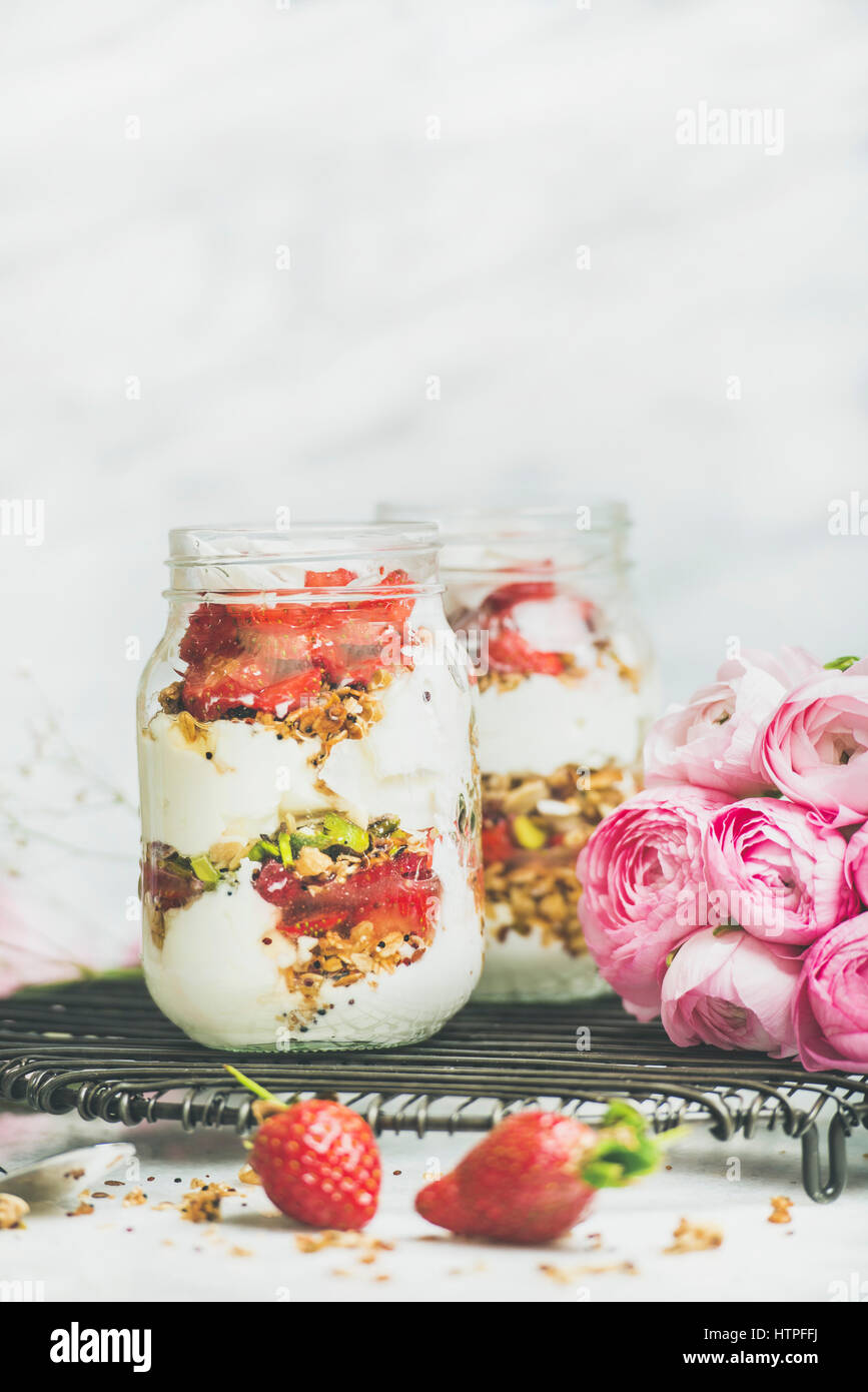 Healthy spring breakfast. Greek yogurt, granola, fresh strawberry breakfast in jars, pink raninkulus flowers, marble background, selective focus, copy Stock Photo
