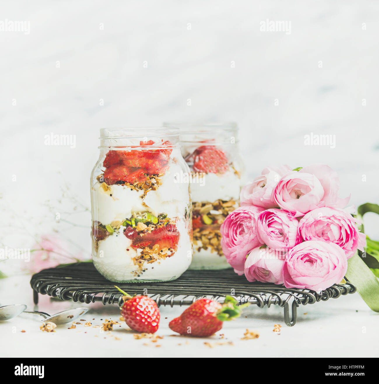 Healthy spring breakfast. Greek yogurt, granola, strawberry breakfast in glass jars, pink raninkulus flowers, marble background, selective focus, copy Stock Photo