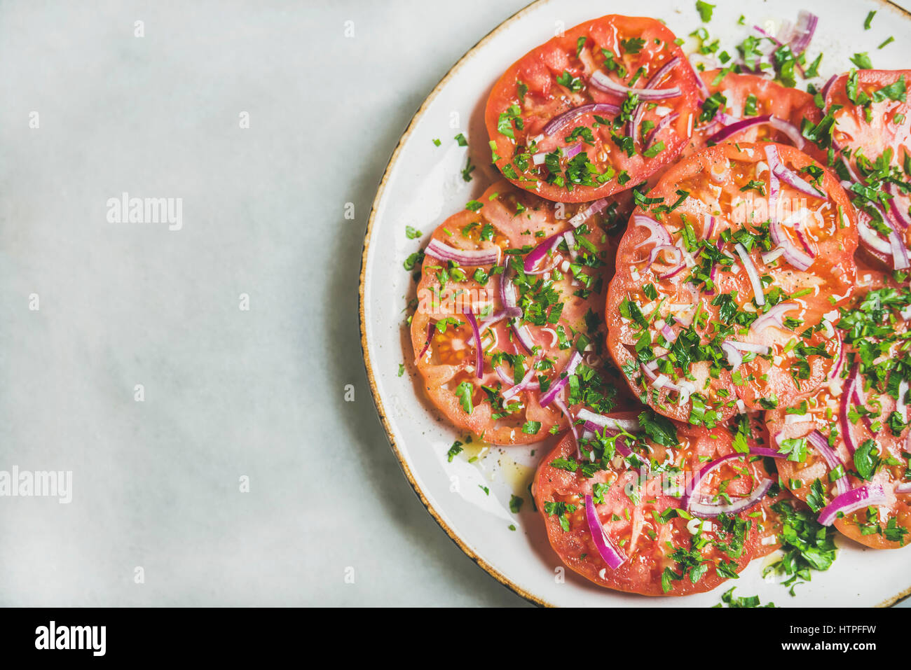 Fresh heirloom tomato, parsley and onion salad in white plate over light grey marble background, top view, copy space. Clean eating, vegan, vegetarian Stock Photo