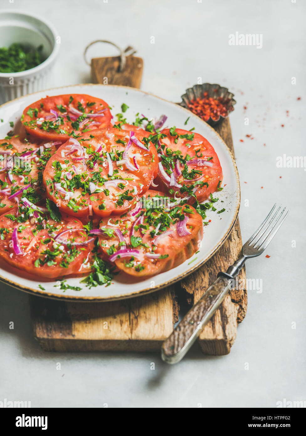 Fresh heirloom tomato, parsley and onion salad in white plate on wooden board over light grey marble background, selective focus. Clean eating, vegan, Stock Photo