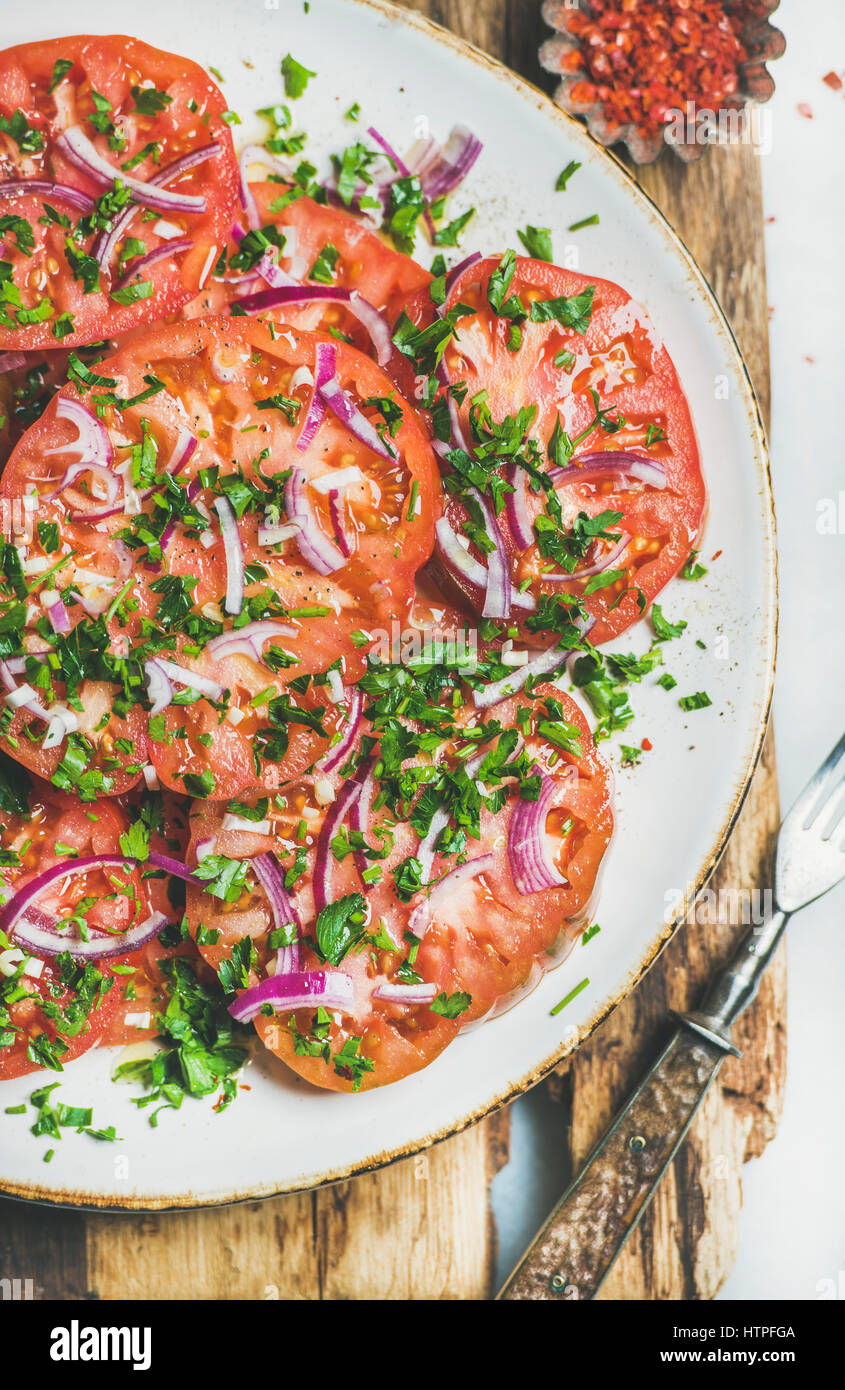 Fresh heirloom tomato, parsley and onion salad in white plate on wooden board over light grey marble background, top view. Clean eating, vegan, vegeta Stock Photo